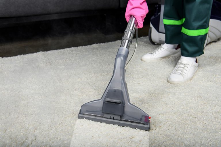 cropped shot of person in rubber glove cleaning carpet with vacuum cleaner
